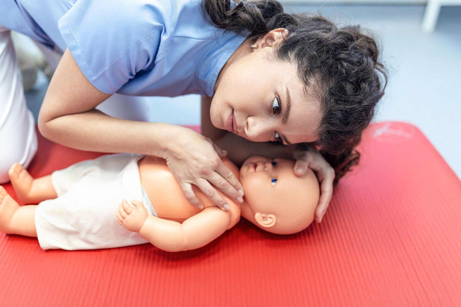 CPR practitioner examining airway passages on infant dummy. Model dummy lays on table and two doctors practice first aid.