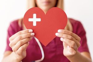 Healthcare worker holding a red heart with a medical cross symbol.
