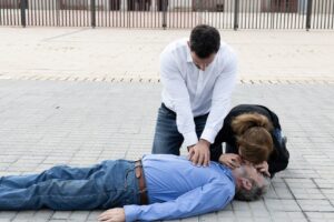 Two bystanders giving CPR and rescue breaths to a man on the ground under Good Samaritan aid
